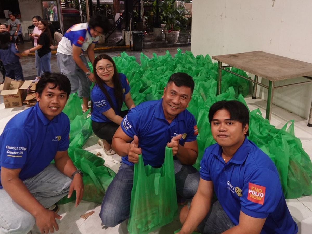 Volunteers kneeling among packed relief bags, thumbs up